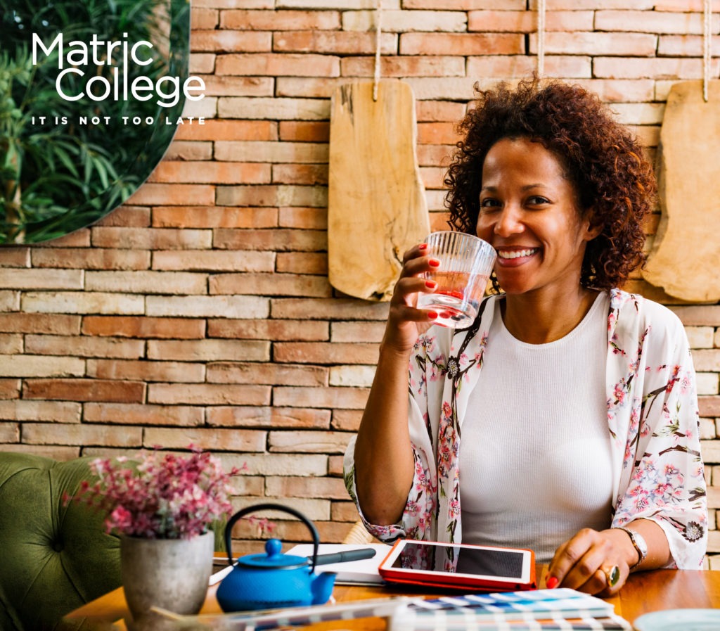 A smiling woman enjoys a drink while studying on a tablet at home, representing confidence and success through Short Courses That Lead To Good Jobs.