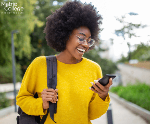 A smiling student wearing a yellow sweater and backpack checks her phone outdoors—thinking about 'How will you finance your studies?