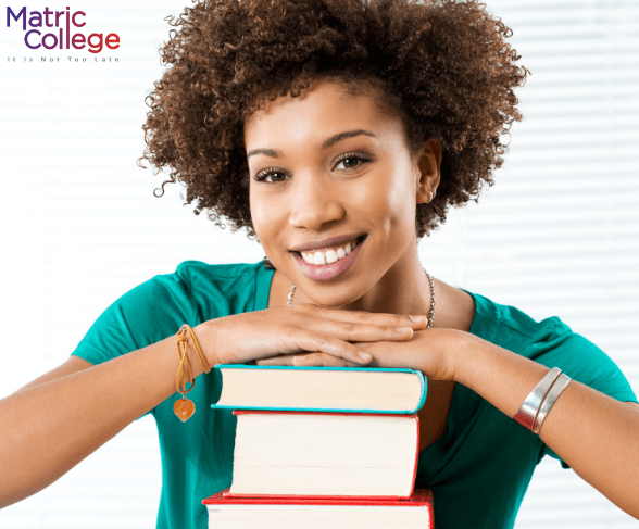 A smiling woman resting her chin on a stack of books, representing success through Adult Matric studies at Matric College.